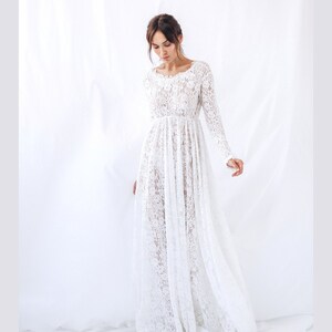 May include: A white lace maxi dress with long sleeves and a scoop neckline. The dress is made of delicate lace and has a flowing silhouette.