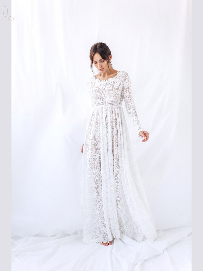 May include: A white lace maxi dress with long sleeves and a scoop neckline. The dress is made of delicate lace and has a flowing silhouette.