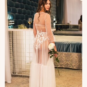 May include: A white sheer maxi dress with delicate floral embroidery and a ruffled hem. The dress is made from a lightweight, flowing fabric and has a fitted bodice.
