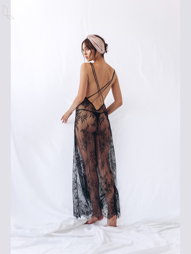 May include: A black lace maxi dress with spaghetti straps and a low back. The dress features a floral pattern and is worn with a matching thong. A light pink headband is also worn.