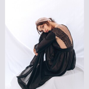May include: A black sheer maxi dress with a lace back detail. The dress is worn by a person with a light brown headband. The person is sitting on a white surface.