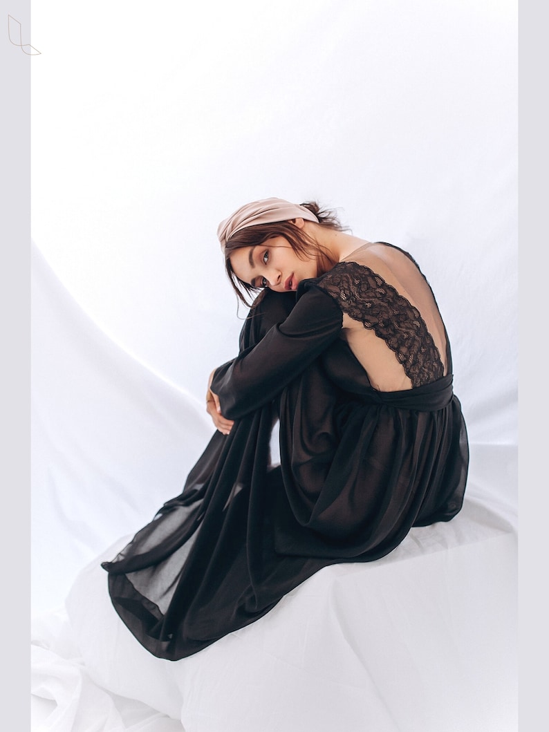 May include: A black sheer maxi dress with a lace back detail. The dress is worn by a person with a light brown headband. The person is sitting on a white surface.