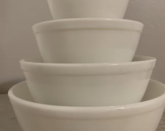 May include: A set of four white ceramic mixing bowls, nested together in size order. The bowls are all plain white with a smooth, glossy finish.