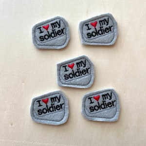 May include: Five gray felt patches with the text "I my soldier" embroidered in black with a red heart in the middle of the text.