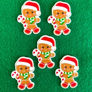 May include: Five gingerbread man stickers on a green background. Each sticker features a gingerbread man wearing a red Santa hat, a green and white scarf, and red shoes, holding a candy cane.