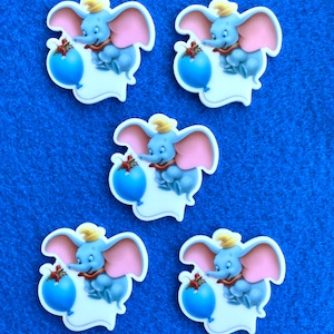 May include: Four colorful resin cabochons featuring a cartoon elephant holding a blue balloon. The elephant is wearing a yellow hat and a red scarf.