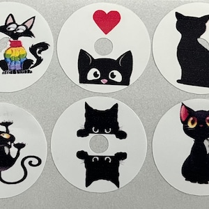 Può includere: Sei adesivi rotondi bianchi con illustrazioni di gatti neri. Gli adesivi presentano diverse pose di gatti, tra cui un gatto che indossa un maglione arcobaleno, un gatto che sbircia da dietro un muro, un gatto seduto con la coda arrotolata, un gatto con un cuore sopra di lui, un gatto che pende a testa in giù e un gatto seduto con la coda arrotolata.