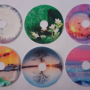 May include: Six round, colorful stickers with a hole in the center. Each sticker features a different nature scene, including a dandelion, a butterfly, a sunset, a lake, and a forest.