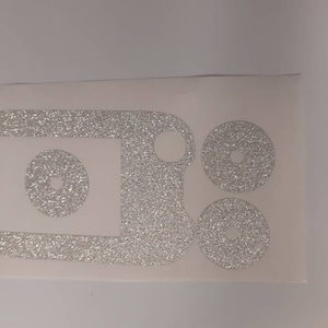 Puede incluir: Un conjunto de calcomanías de vinilo plateado con purpurina para una funda de teléfono. El conjunto incluye un rectángulo grande con un círculo en el interior y dos círculos más pequeños.