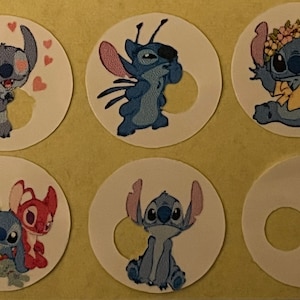 Op de afbeelding: Zes ronde stickers met het personage Stitch uit de Disney-film Lilo & Stitch. Elke sticker toont Stitch in verschillende poses, met verschillende uitdrukkingen en accessoires, waaronder harten en een bloemenkrans. De stickers staan op een lichtgele achtergrond.