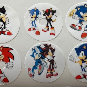 May include: Six round stickers featuring different characters from the Sonic the Hedgehog video game franchise. The stickers feature Sonic, Shadow, and Knuckles in various poses. The stickers are white with a hole in the centre.