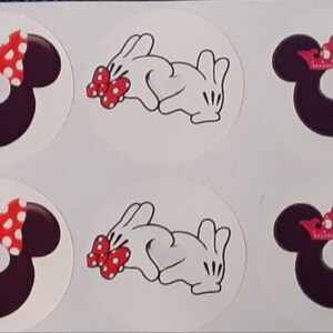 Può includere: Sei adesivi rotondi con diversi personaggi Disney. Gli adesivi mostrano le orecchie di Topolino con un fiocco rosso, le orecchie di Topolino con una corona rosa e i guanti di Topolino con un fiocco rosso.