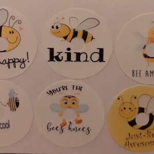 May include: Six round stickers featuring bee illustrations and positive messages. The stickers depict bees with black and yellow stripes, wings, and smiling faces. The messages include "bee happy!", "kind", "bee amazing", "bee cool", "you're the bees knees", and "just-bee awesome!"