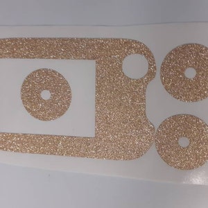 May include: A set of four gold glitter vinyl stickers for a device. The stickers are in the shape of circles and a rectangle. The stickers are designed to cover the buttons and screen of a device.
