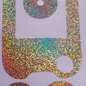 以下が含まれることがあります： ホログラフィック仕上げのゴールドグリッターステッカー4枚セット。 ステッカーはキーホルダーの形で、中央に丸い穴があります。