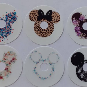 Puede incluir: Seis pegatinas redondas blancas con un diseño de silueta de Mickey Mouse. Cada pegatina presenta un patrón diferente, incluyendo flores, estampado de leopardo y confeti.