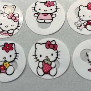 May include: Eight round stickers featuring Hello Kitty in various poses and outfits. The stickers are white with a pink border and Hello Kitty is depicted in pink, red, and black.
