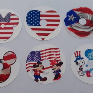 Può includere: Sei adesivi rotondi con diversi design patriottici. Gli adesivi presentano Topolino, Minnie Mouse, Trilly, Snoopy e la bandiera americana. Gli adesivi sono tutti bianchi con design rosso, bianco e blu.
