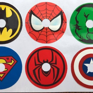 Peut inclure: Six autocollants ronds représentant des logos de super-héros. Les autocollants sont rouges, bleus, jaunes, verts et noirs. Les logos incluent Batman, Superman, Spiderman, Hulk et Captain America.