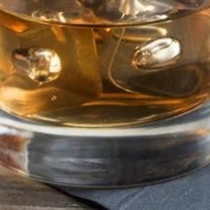 a glass of whiskey with ice cubes on a wooden table