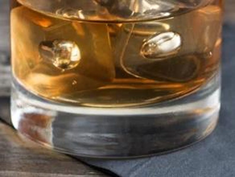 a glass of whiskey with ice cubes on a wooden table