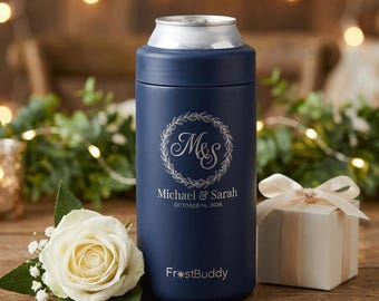 May include: Navy blue can cooler with a silver rim, featuring a floral wreath design with the initials "M&S" and the names "Michael & Sarah" and the date "October 14, 2026". A white rose and gift box are in the foreground.