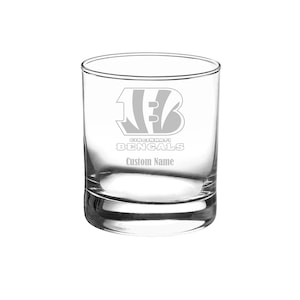 May include: A clear glass tumbler with an etched design of the Cincinnati Bengals logo and the team name. The text "Custom Name" is also etched on the glass.