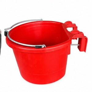 Może przedstawiać: Jaskrawoczerwone plastikowe wiadro z płaską tylną stroną wyposażoną w trzy zintegrowane haczyki do montażu. Wiadro posiada srebrny metalowy uchwyt z czarnymi plastikowymi nakładkami w punktach mocowania, przeznaczone do zawieszenia na ogrodzeniu.
