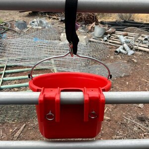 Może przedstawiać: Jaskrawoczerwone plastikowe wiadro z metalowym uchwytem i dwoma zintegrowanymi haczykami do montażu. Wiadro jest zawieszone na poziomej metalowej poprzeczce za pomocą czarnego nylonowego paska z metalowym klipsem i posiada dwa małe srebrne pierścienie.