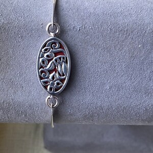 May include: A silver bracelet with a red oval charm featuring a floral design.