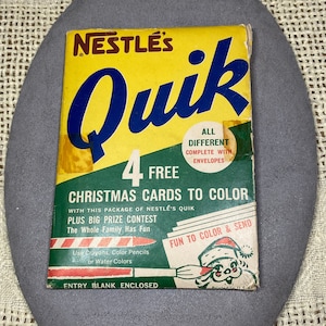 Puede incluir: Una caja amarilla y verde con las palabras "Nestle's Quik" y "4 tarjetas de Navidad gratis para colorear" impresas en ella. La caja incluye un formulario de participación en el concurso e instrucciones para usar crayones, lápices de colores o acuarelas.