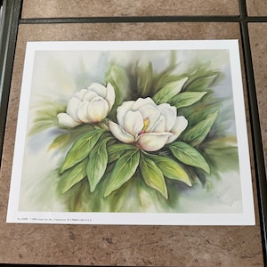 May include: A watercolor painting of two white magnolia flowers with green leaves. The painting is signed "Alice Levine" in the bottom right corner. The text "No. 52498 - 1996 Grand Art, Inc., Vancouver, WA 98660 Little Lake, U.S.A." is printed in the bottom left corner.