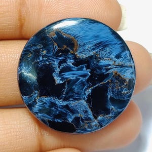Puede incluir: Un cabuj&oacute;n redondo de ojo de tigre azul y dorado. La piedra tiene un patr&oacute;n de remolino de azul y dorado.