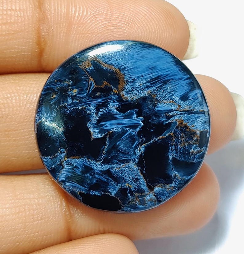 Puede incluir: Un cabuj&oacute;n redondo de ojo de tigre azul y dorado. La piedra tiene un patr&oacute;n de remolino de azul y dorado.