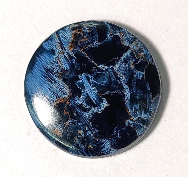 Puede incluir: Un cabuj&oacute;n redondo de ojo de tigre azul y dorado. La piedra tiene un patr&oacute;n de remolino de azul y dorado.