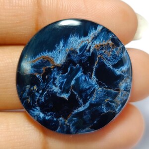 Puede incluir: Un cabuj&oacute;n redondo de ojo de tigre azul y dorado. La piedra tiene un patr&oacute;n de remolino de azul y dorado.