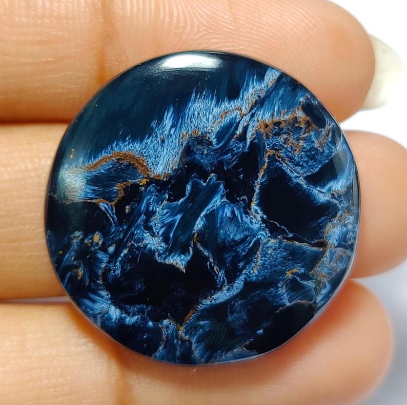 Puede incluir: Un cabuj&oacute;n redondo de ojo de tigre azul y dorado. La piedra tiene un patr&oacute;n de remolino de azul y dorado.