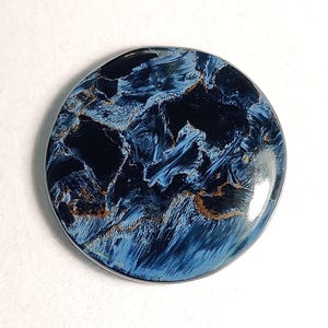 Puede incluir: Un cabuj&oacute;n redondo de ojo de tigre azul y dorado. La piedra tiene un patr&oacute;n de remolino de azul, negro y dorado.