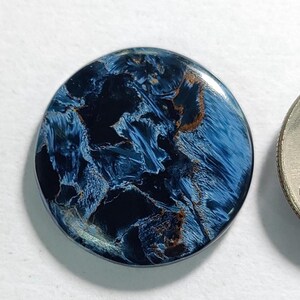 Puede incluir: Un cabuj&oacute;n redondo de ojo de tigre azul y dorado. La piedra tiene un patr&oacute;n de remolino de azul y dorado.