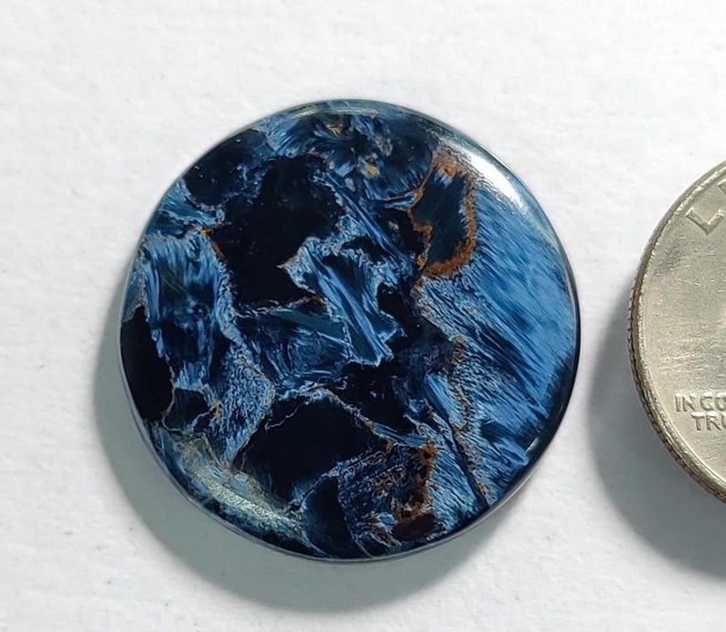 Puede incluir: Un cabuj&oacute;n redondo de ojo de tigre azul y dorado. La piedra tiene un patr&oacute;n de remolino de azul y dorado.