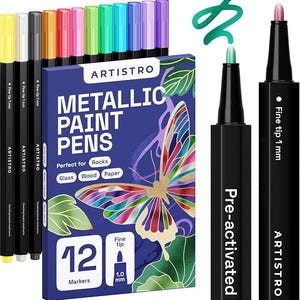 Op de afbeelding: Een set van twaalf Artistro metallic verfstiften met 1 mm fijne punten, in een blauwe doos met een vlinderillustratie. De set bevat diverse gekleurde markers en twee zwarte pennen zijn afgebeeld zonder dop om de punten te tonen.