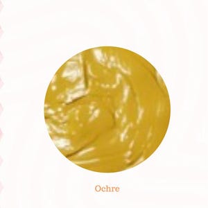 May include: A circular swatch of ochre-colored paint. The paint has a textured, swirled appearance. The word "Ochre" is printed in a simple font below the paint swatch. The background is white with a pink decorative border.