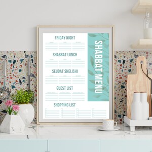 May include: A framed "Shabbat Menu" print with a light wood frame. The menu features sections for Friday night, Shabbat lunch, Seudat Shelishi, a guest list, and a shopping list. The background is white with a teal accent.