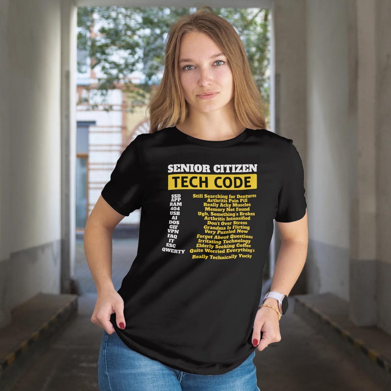 May include: Black t-shirt with the text "SENIOR CITIZEN TECH CODE" in yellow and white. The shirt lists tech-related acronyms and their humorous meanings, such as "SSD: Still Searching for Dentures."