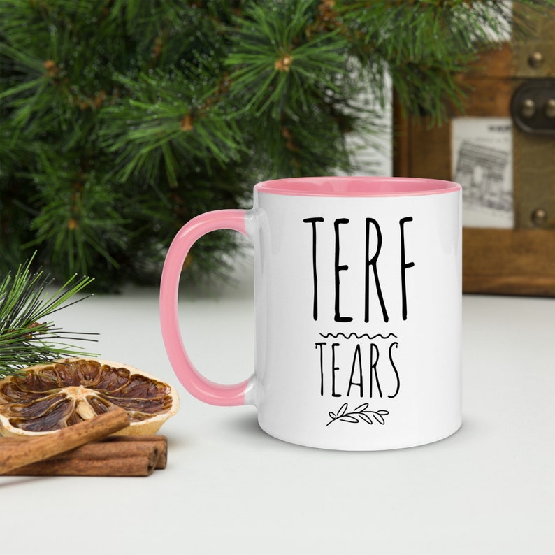 May include: White ceramic mug with a pink rim and handle. The mug has black text that reads "TERF TEARS" with a small floral design underneath.