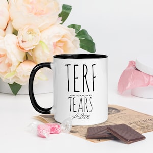 May include: White ceramic mug with a black rim and handle. The mug has black text that reads "TERF TEARS" with a small branch design below the text.