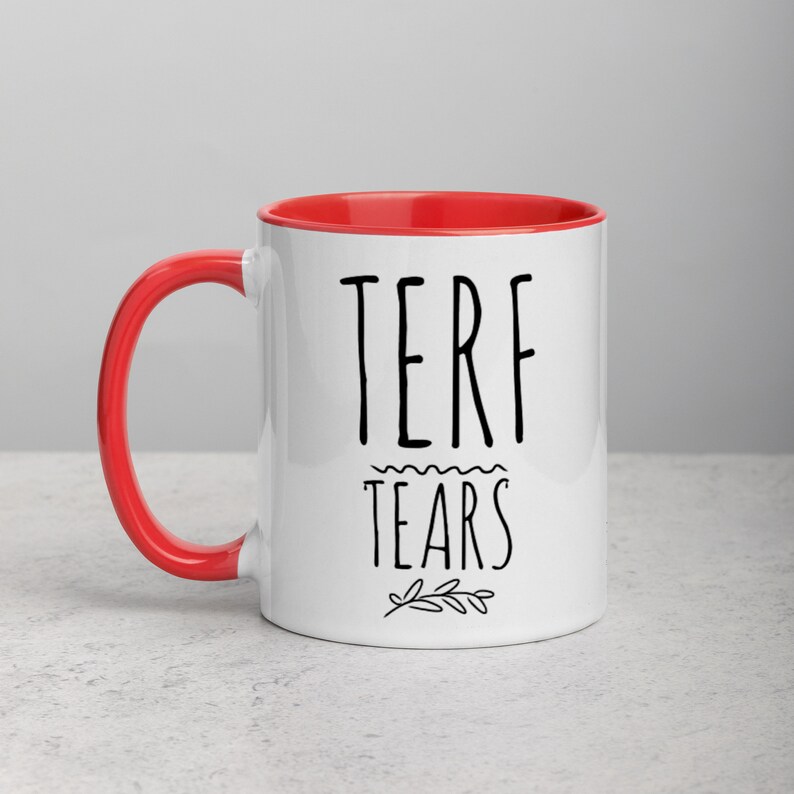 May include: White ceramic mug with a red rim. The mug has black text that reads "TERF TEARS" with a small floral design below the text.
