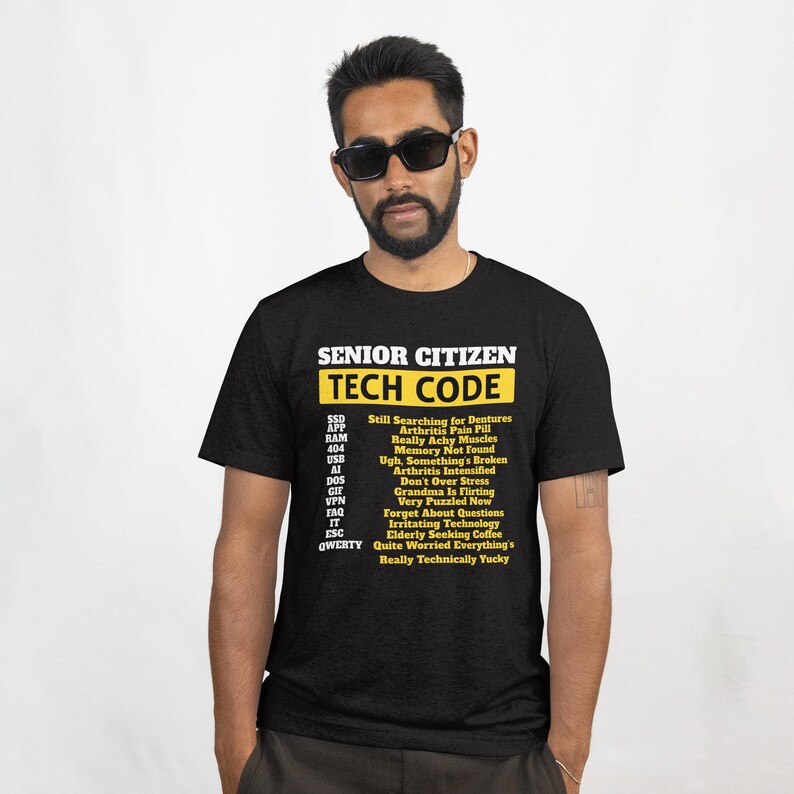 May include: Black t-shirt with the text "SENIOR CITIZEN TECH CODE" in white and yellow. The shirt lists humorous tech-related phrases like "Memory Not Found" and "Arthritis Intensified".