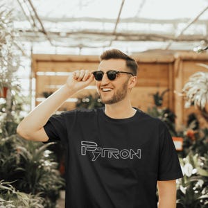 Puede incluir: Un hombre con gafas de sol y una camiseta negra con la palabra "PYTRON" impresa en blanco en la parte delantera.