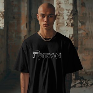Puede incluir: Una camiseta negra con un contorno blanco de la palabra "PYRON" en la parte delantera. El modelo lleva una cadena de plata.